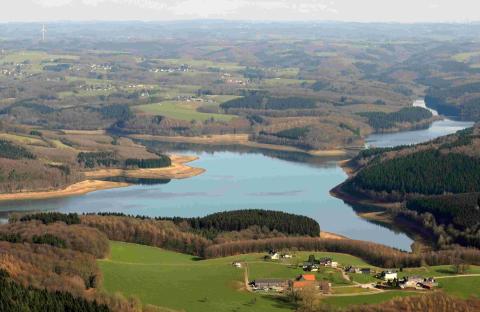 Luftbild aus großer Höhe auf einen See, hügelige Landschaft, Wiesen, Wälder, Dorf