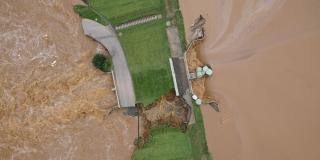 Luftbild auf ein mit Gras bewachsenes Bauwerk, das beinah von schlammigem Hochwasser überflutet und zerstört wird