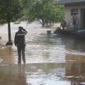 überflutete Straße, Menschen, angeschwemmte Gegenstände, Haus und Bäume, die aus dem Wasser ragen
