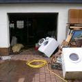 Garageneinfahrt eines Hauses vor dem kaputte Hausshaltsgeräte und Möbel aufgestapelt sind, Schlauch