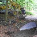Das Foto zeigt einen Bagger an einem neu hergestellten Gewässerdurchlass unter einem Wirtschaftsweg im Wald